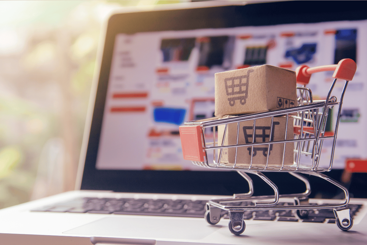 Laptop with online shopping and a small shopping cart with boxes on top